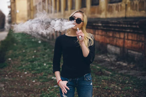 Vaping. Young beautiful woman smoking ( vaping ) e-cigarette with smoke outdoors. Vapor concept. — Stock Photo, Image