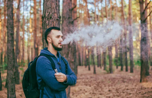 Vapeado. Hombres casuales con barba vapeando un cigarrillo electrónico. Vapeando al aire libre en el bosque. Fumar seguro. Vaper joven . — Foto de Stock