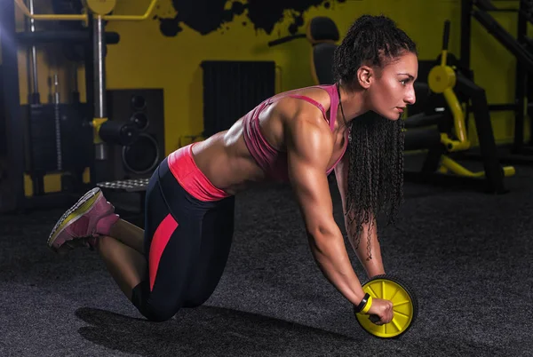 Mujer atractiva haciendo ejercicio con rodillo de rueda para abdominales en el suelo en el gimnasio como parte del entrenamiento de fitness — Foto de Stock
