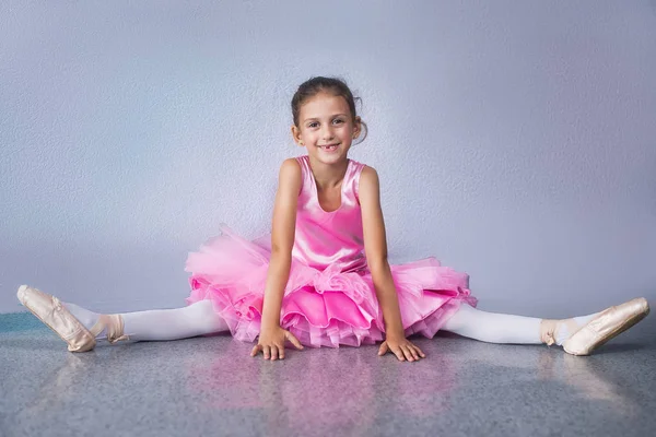 Junge Ballerina in pinkfarbenen Kleidern sitzt während des Tanzkurses auf dem Boden. — Stockfoto