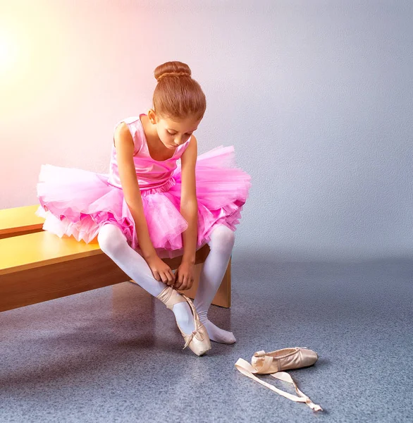 Молодая балерина в розовой одежде сидит на скамейке во время тренировки в танцевальном классе . — стоковое фото