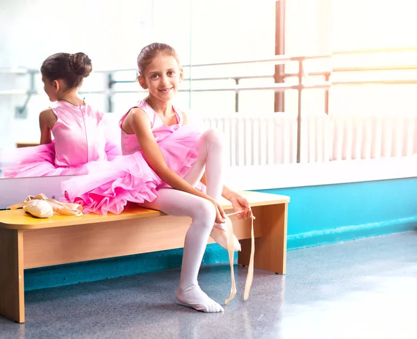 Mladá baletka v růžových šatech sedí na lavičce během výcviku v taneční třídě. — Stock fotografie