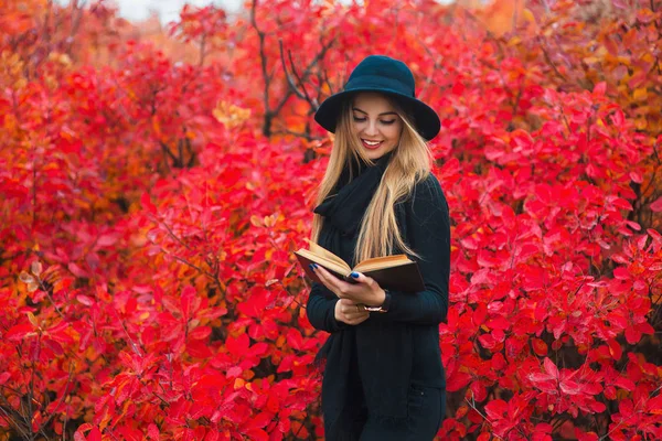在黑色的帽子，在公园里看书的年轻女人。秋天的肖像 — 图库照片