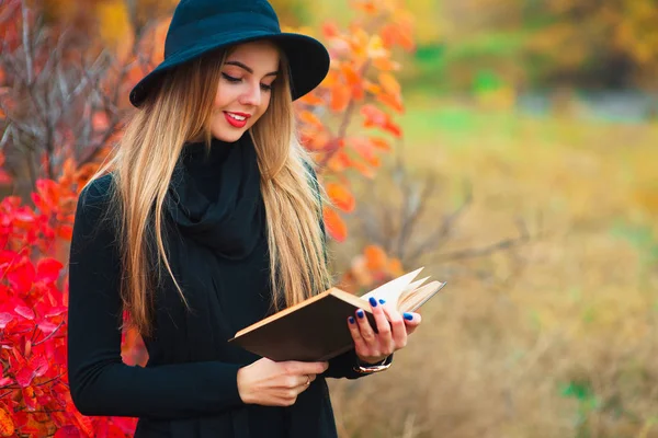 在黑色的帽子，在公园里看书的年轻女人。秋天的肖像 — 图库照片