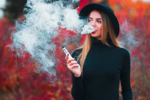 Vapor. Jovem mulher bonita em chapéu vaping ao ar livre no outono — Fotografia de Stock