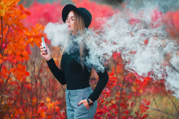 Vapor. Jovem mulher bonita em chapéu vaping ao ar livre no outono — Fotografia de Stock