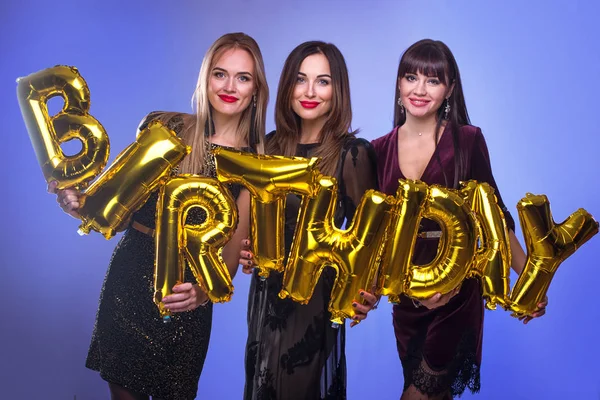 Three beautiful elegant women celebrate birthday and holding balloons in the form of inscription birthay. People celebrate the holiday