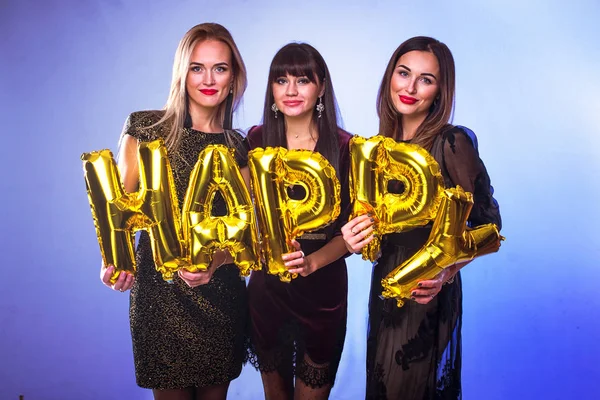 Three beautiful elegant women celebrate birthday and holding balloons in the form of inscription Happy. People celebrate the holiday
