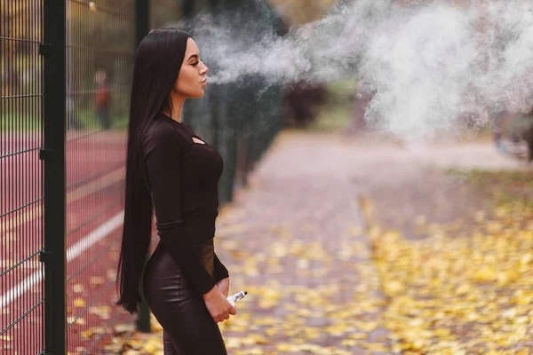 Sexig kvinna vaping elektronisk vattenpipa utomhus på hösten. Vape godsaker — Stockfoto