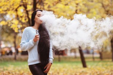 Vaping. Genç güzel kadın vaping ile duman açık havada. Buharı kavramı.