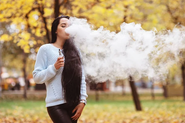 Вэйпинг. Молодая красивая женщина испаряется дымом на улице. Концепция пара . — стоковое фото