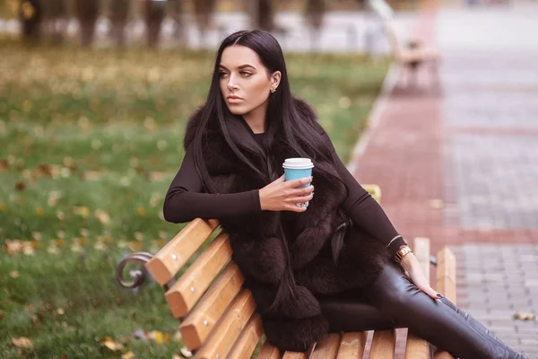 Mujer disfrutar de la temporada de otoño sentado en el banco blanco en el parque de otoño y el café de calentamiento dring. Hojas amarillas y naranjas — Foto de Stock