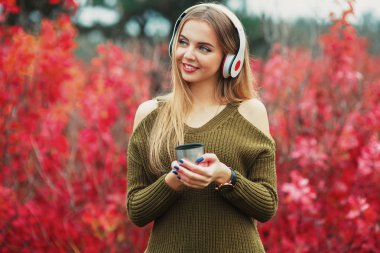 Fincan çay, kulaklık ve smartphone Park'ta açık havada duran gülümseyen güzellik genç kızla