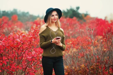 zevk, denim kıyafeti, gülümseyen, mutlu, genç yenilikçi şık güzel kız dinleme müzik, cep telefonu, kulaklık, cool aksesuarları, vintage tarzı, eğleniyor, gülüyor, park