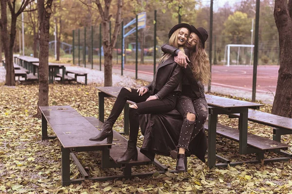 Portrait de deux belles jeunes copines en chapeaux noirs assis sur banc rire et s'amuser — Photo