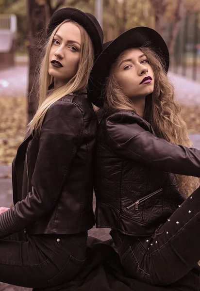 Primer plano retrato de dos hermosas amigas mujeres jóvenes en ropa de otoño / invierno que usan al aire libre. El uso de abrigo de cuero elegante, jean negro y sombrero casual negro . —  Fotos de Stock