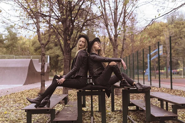 Retrato de duas belas namoradas em chapéus pretos sentado no banco rir e se divertir — Fotografia de Stock