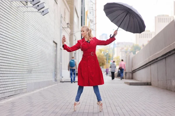 Женщина-балерина держит смартфон и зонтик в городе — стоковое фото