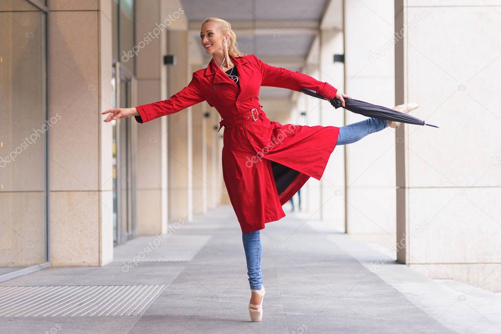 ballerina with umbrella in one hand. Warm autumn day. Woman in red coat and blue jeans