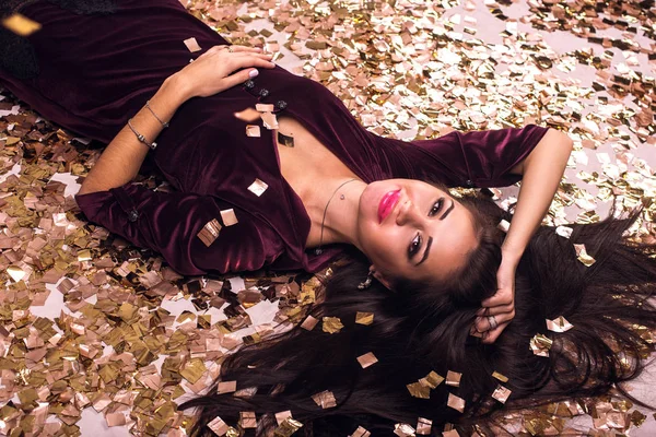 Mujer rubia feliz yace en el suelo en confeti en todas partes. Año nuevo y concepto holliday — Foto de Stock