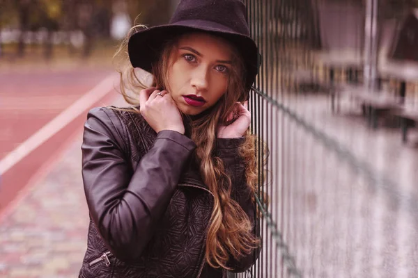Retrato de mujer joven rubia atractiva en sombrero fedora negro y chaqueta de cuero mirando a la cámara — Foto de Stock