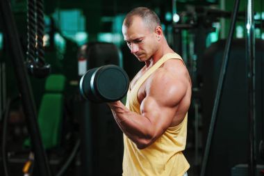 Atletik gömleksiz genç spor adamı - fitness modeli halter salonunda tutar. Kopya alanı metin ön plana.