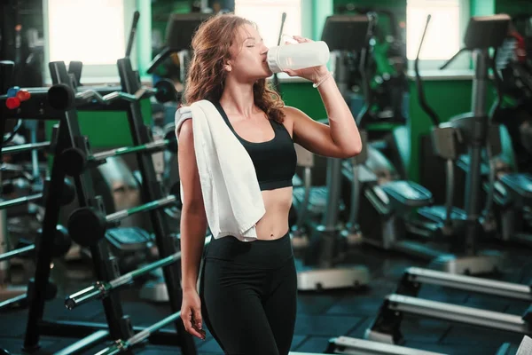 Atractiva mujer joven bebiendo proteínas en el gimnasio —  Fotos de Stock