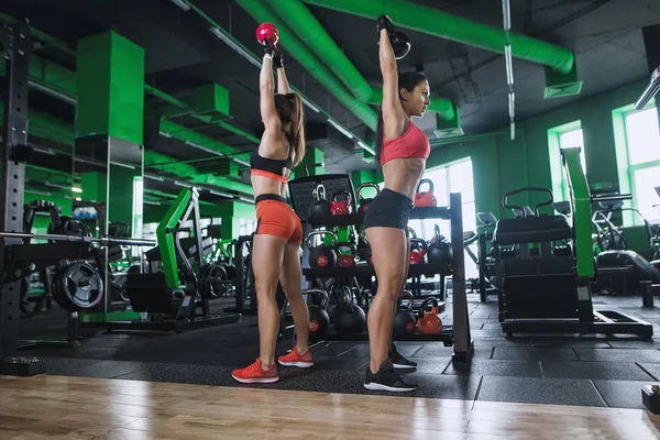 Functional fitness workout in sport gym. Two woman with kettlebell