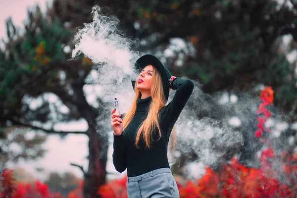 Vaping. Şapka vaping açık havada sonbaharda genç güzel kadın