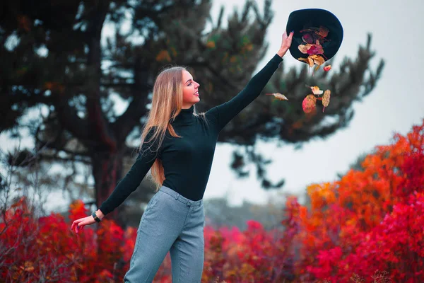 Mujer joven en hermoso parque de otoño, hojas que caen del sombrero, concepto otoño — Foto de Stock