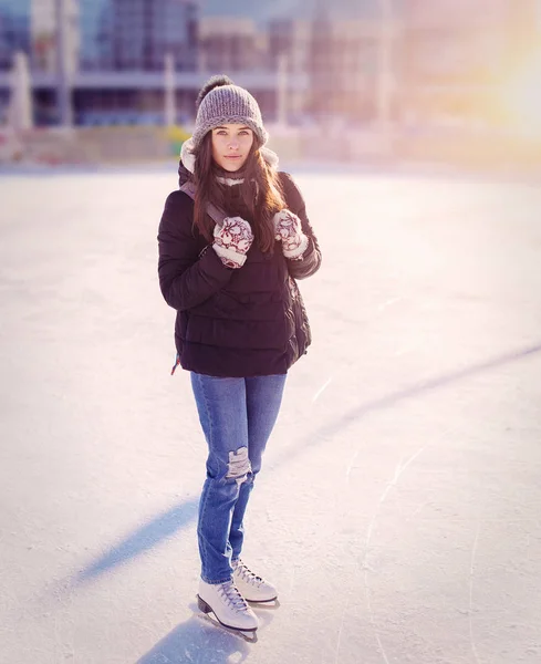 Young woman ice skating outdoors on ice rink in winter day