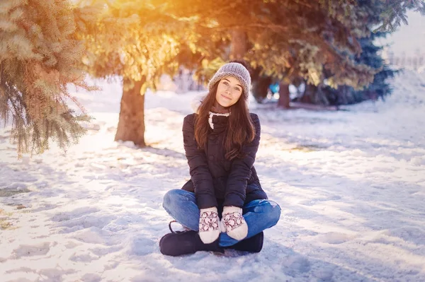 冬帽子手袋とスカーフを身に着けている美しい幸せな笑っている若い女は雪の結晶で覆われています。冬の森の風景の背景 — ストック写真