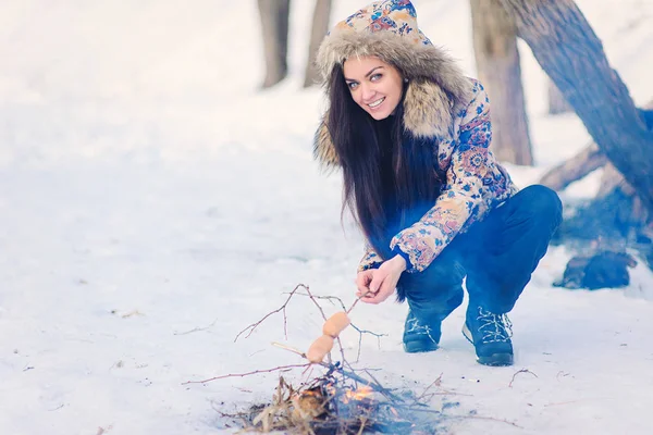 冬の森の中でたき火フライ ソーセージの近くの女性 — ストック写真