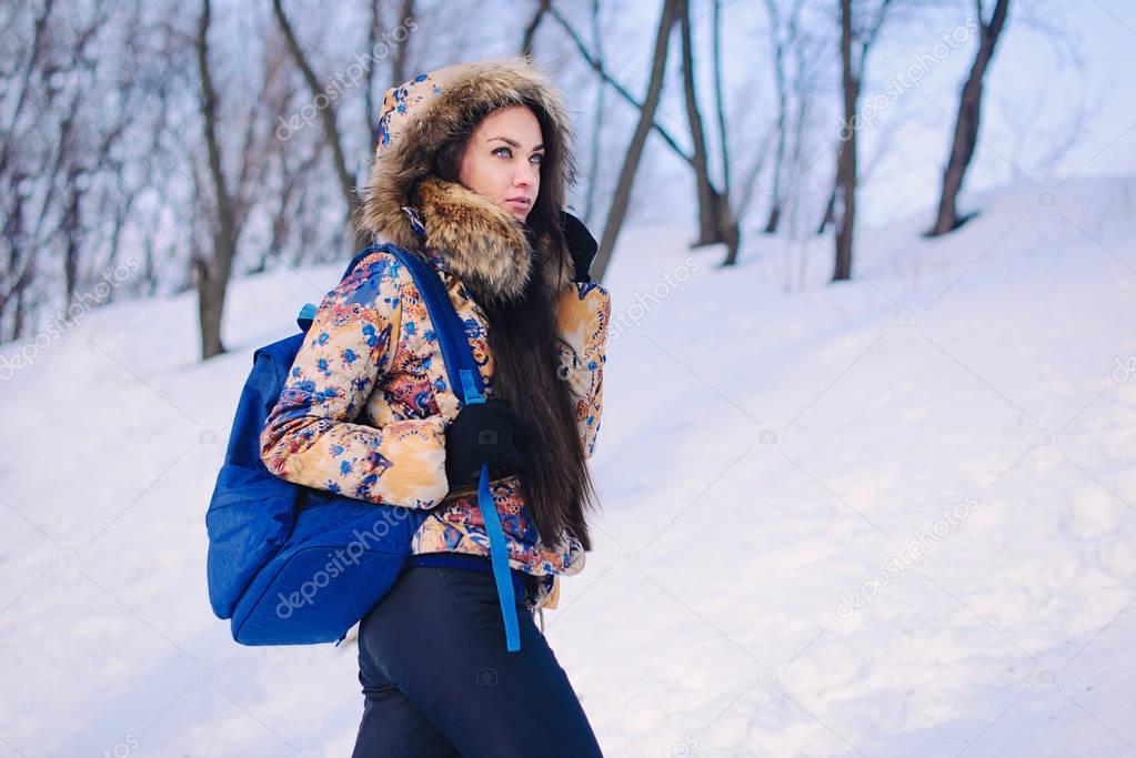 Beautiful young woman spending time in winter forest. Wearing coat and backpack. Winter is coming, first snowfall.