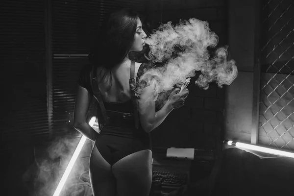 Giovane bella donna bruna fumare, vaping e-sigaretta con fumo su sfondo nero . — Foto Stock