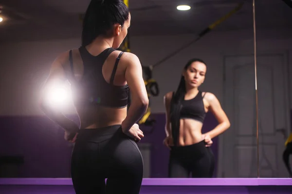 Mujer mirando al espejo sintiéndose feliz y satisfecha después del entrenamiento en un gimnasio — Foto de Stock