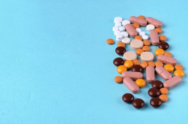 Çeşitli ilaç hapları, haplar ve kapsüller mavi arka planda.