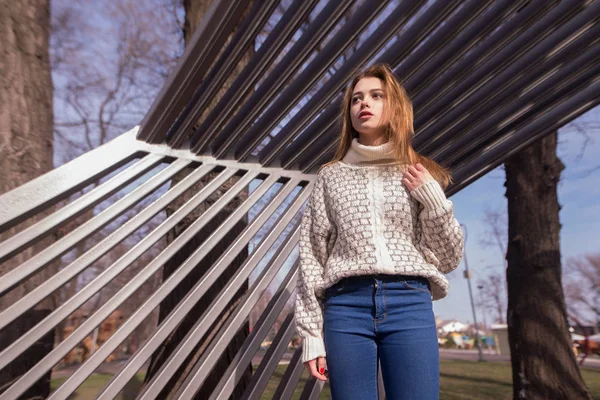 Portrét mladé ženy oblečené v pletený svetr a džíny. Stojící poblíž plotové konstrukce kovové perforované parkování — Stock fotografie