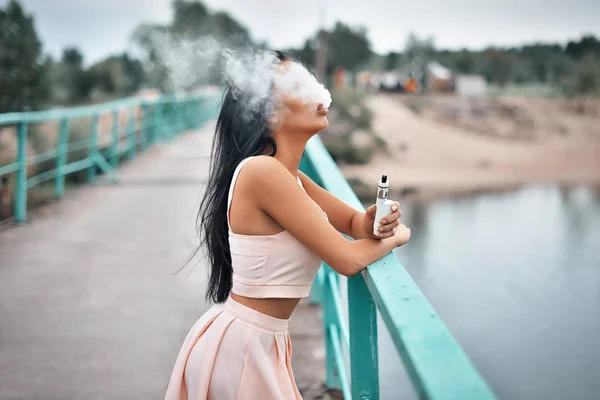 Menguap. Wanita muda cantik merokok (uap) e-rokok dengan asap di luar ruangan. Konsep uap . — Stok Foto
