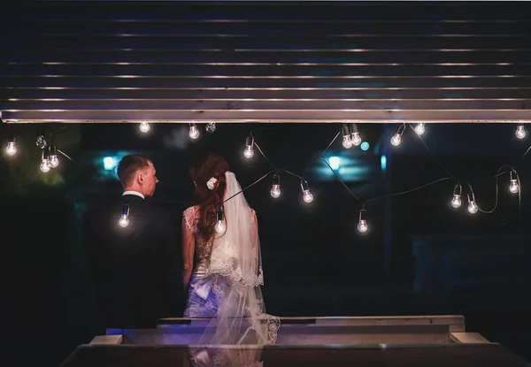 Enamored newlyweds gently embrace. Wedding ceremony in nature. The lights of the electric garland illuminate the wedding party.