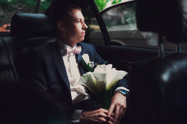Przystojny pan młody siada z Bukiet ślubny wewnątrz samochodu i wygląd w oknie poza — Zdjęcie stockowe