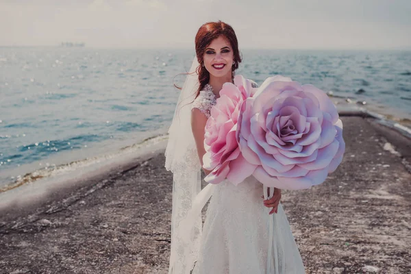 Gyönyörű menyasszony kezében nagy papír virágok-tenger közelében — Stock Fotó