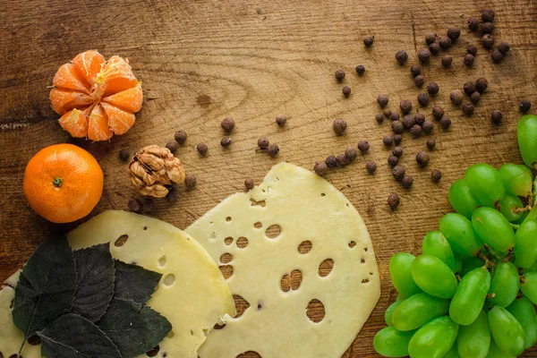 Bandeja de queso con diferentes quesos, uvas, frutos secos, miel y dátiles sobre fondo rústico de madera. Selección de variedades de queso estilo retro en tablero de madera . — Foto de Stock