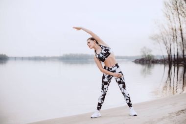 Sahilde germe egzersiz yaparak güzel rakam ile ince kadın avcısı, sabah çalıştırmak, fitness ve sağlıklı yaşam konsepti