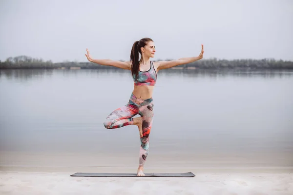 Sportovní žena cvičí jógu na pláži ráno. Žena stojí na jógu — Stock fotografie