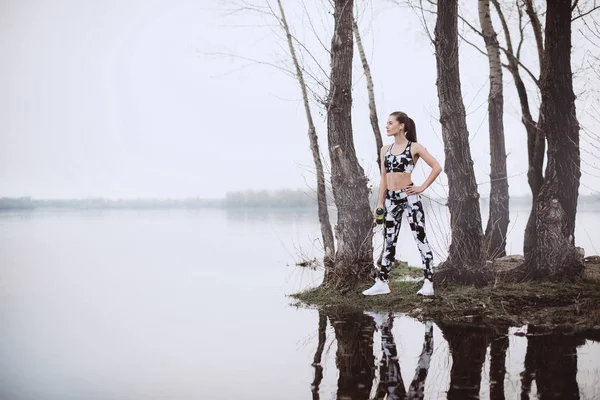 Sporty woman standing near the river at morning sunrise . Fit woman rest after jogging. Morning run