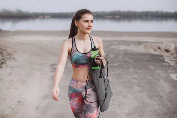 Atlama ipi, yoga mat ve eğitim parkta yürürken elinde tutan sportif kadın. Güzel sportif fitness modeli açık egzersiz sırasında.