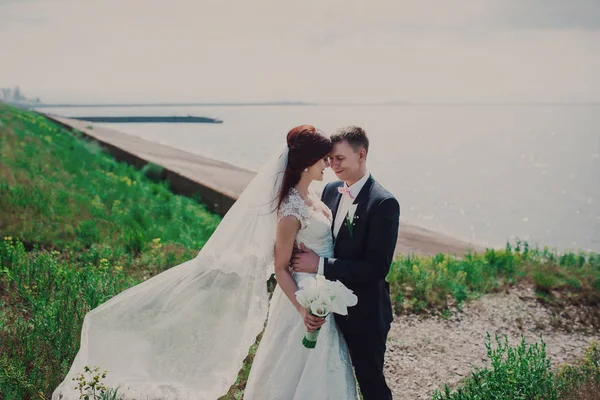 Gyönyörű esküvői r. az ifjú a tó közelében áll. menyasszony, egy fényűző ruhát és egy gyönyörű csokor — Stock Fotó