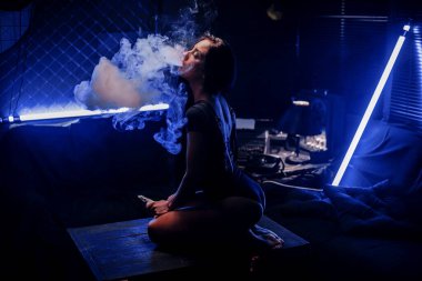 Vaping aleti olan seksi bir kadın nikotin sigarası yerine e-sıvı içiyor. Tütünsüz e-meyve suyu. Vaping konsepti. Modern kız tüttürüyor.