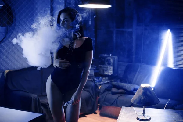 Vaping aleti olan seksi bir kadın nikotin sigarası yerine e-sıvı içiyor. Tütünsüz e-meyve suyu. Vaping konsepti. Modern kız tüttürüyor.